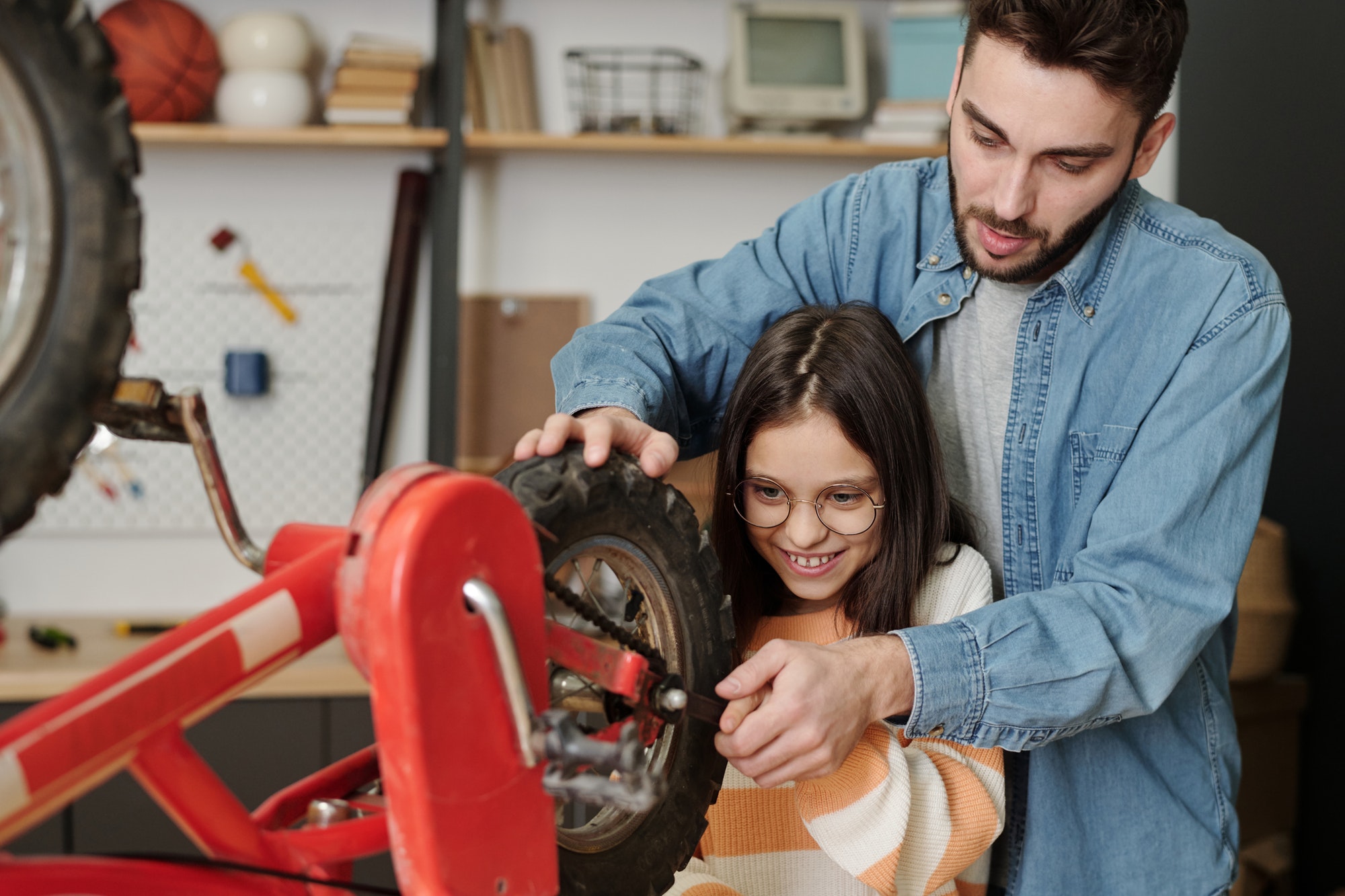 Smiling girl helping father repair her bicycle while holding part of wheel